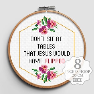May include: Cross-stitch embroidery in a wooden hoop. The design features the text "DON'T SIT AT TABLES THAT JESUS WOULD HAVE FLIPPED" in black and red. Floral accents in pink and green surround the text. The hoop is 8 inches (20 cm) in diameter.