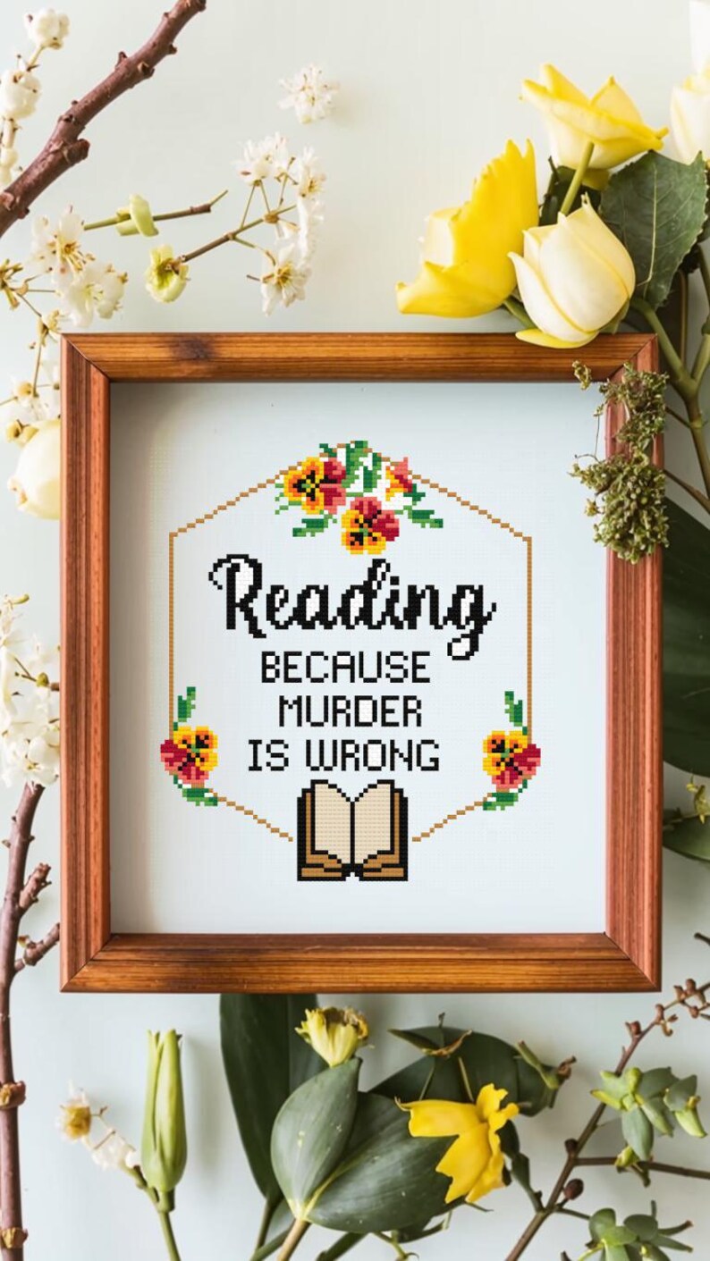 May include: A framed cross-stitch design with a white background and a hexagonal border of yellow and orange flowers. The text reads "Reading because murder is wrong" with a book illustration below.