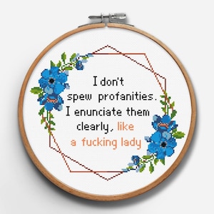 Puede incluir: Un bastidor de bordado de punto de cruz con el texto "I don't spew profanities. I enunciate them clearly, like a fucking lady." El diseño incluye detalles florales azules y un borde geométrico.