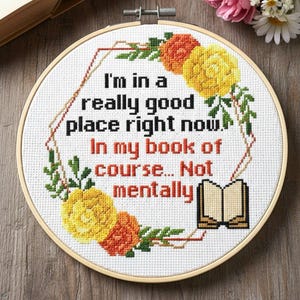 Op de afbeelding: Een borduurwerk in een cirkel met de tekst "I'm in a really good place right now. In my book of course... Not mentally." Het ontwerp bevat gele, oranje en groene bloemen op een witte achtergrond.