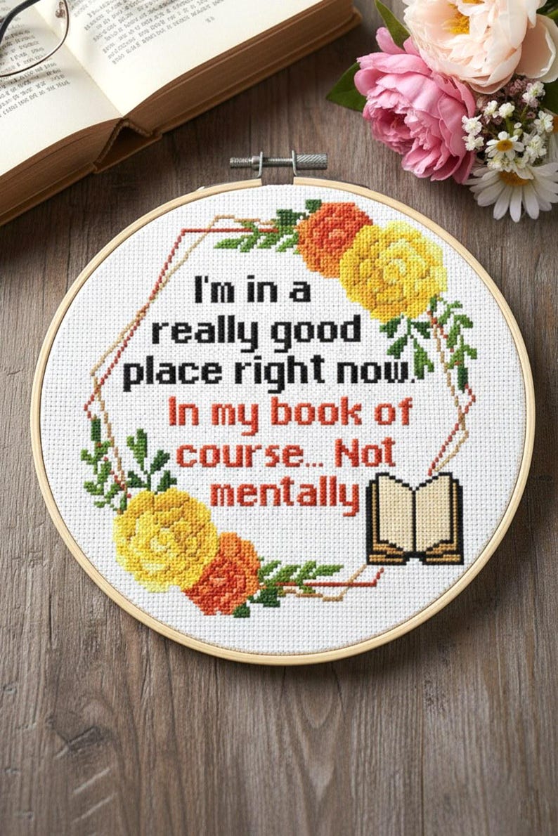 Op de afbeelding: Een borduurwerk in een cirkel met de tekst "I'm in a really good place right now. In my book of course... Not mentally." Het ontwerp bevat gele, oranje en groene bloemen op een witte achtergrond.