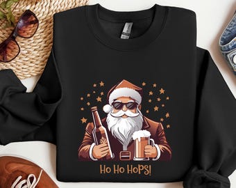 May include: Black sweatshirt with a cartoon Santa Claus wearing sunglasses, holding a beer bottle and a pint of beer. The text "Ho Ho Hops!" is printed below the image. The design includes brown, white, and gold accents.