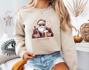 May include: Beige sweatshirt featuring a cartoon Santa Claus wearing sunglasses, holding a beer bottle and a pint of beer. The text "Ho Ho Hops!" is below the graphic. The sweatshirt has long sleeves.