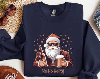 May include: Navy blue sweatshirt with a cartoon Santa Claus wearing sunglasses, holding a beer bottle and a pint of beer. The text "Ho Ho Hops!" is below the image, with orange stars in the background.