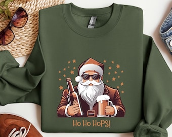 May include: Green sweatshirt with a cartoon Santa Claus wearing sunglasses, holding a beer bottle and a pint of beer. The text "Ho Ho Hops!" is printed below the image. The design includes brown, white, and orange accents.