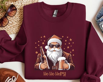 May include: Burgundy crew neck sweatshirt with a cartoon Santa Claus wearing sunglasses, holding a beer bottle and a pint of beer. The text "Ho Ho Hops!" is printed below the graphic. The design includes gold stars.