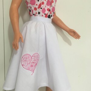 May include: White skirt with a pink embroidered heart design. The skirt is a-line and has a wide waistband.
