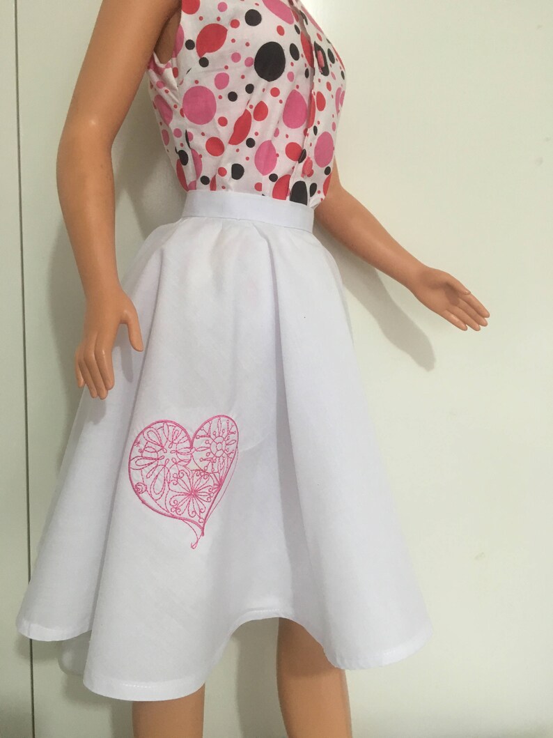 May include: White skirt with a pink embroidered heart design. The skirt is a-line and has a wide waistband.