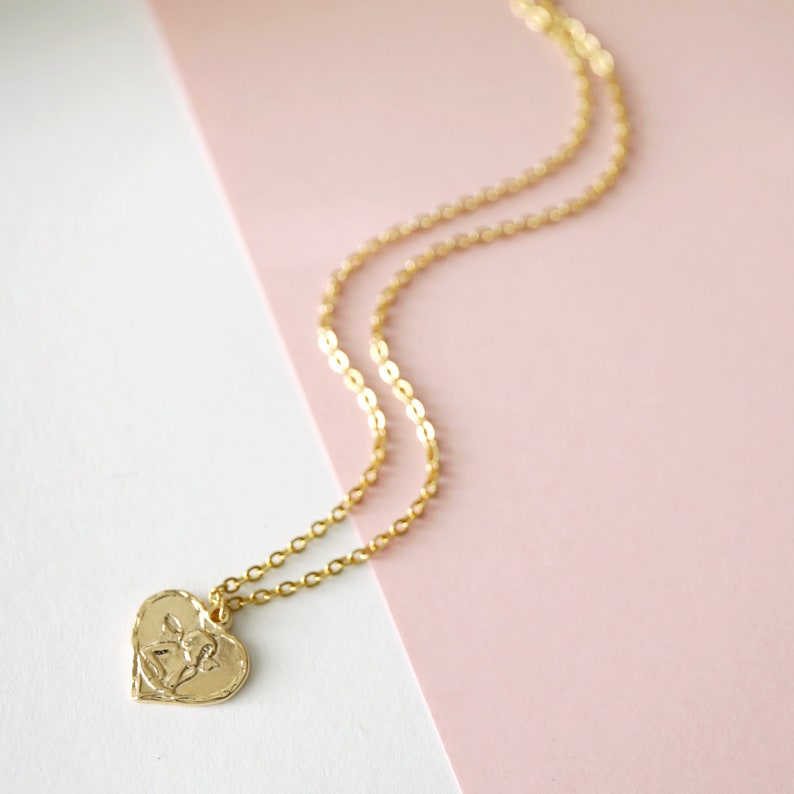 May include: A gold chain necklace with a heart-shaped pendant featuring a floral design.