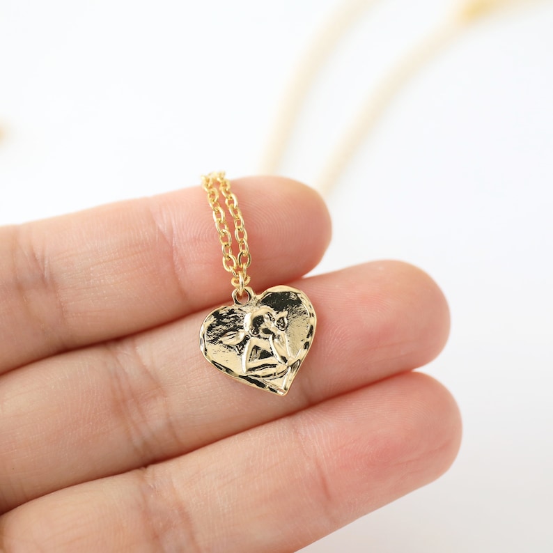 May include: Gold necklace with a heart-shaped pendant featuring an angel design.