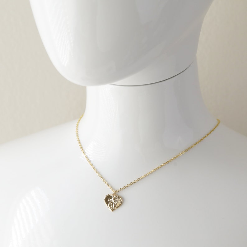 May include: A gold chain necklace with a delicate heart pendant. The heart pendant has a detailed, intricate design.