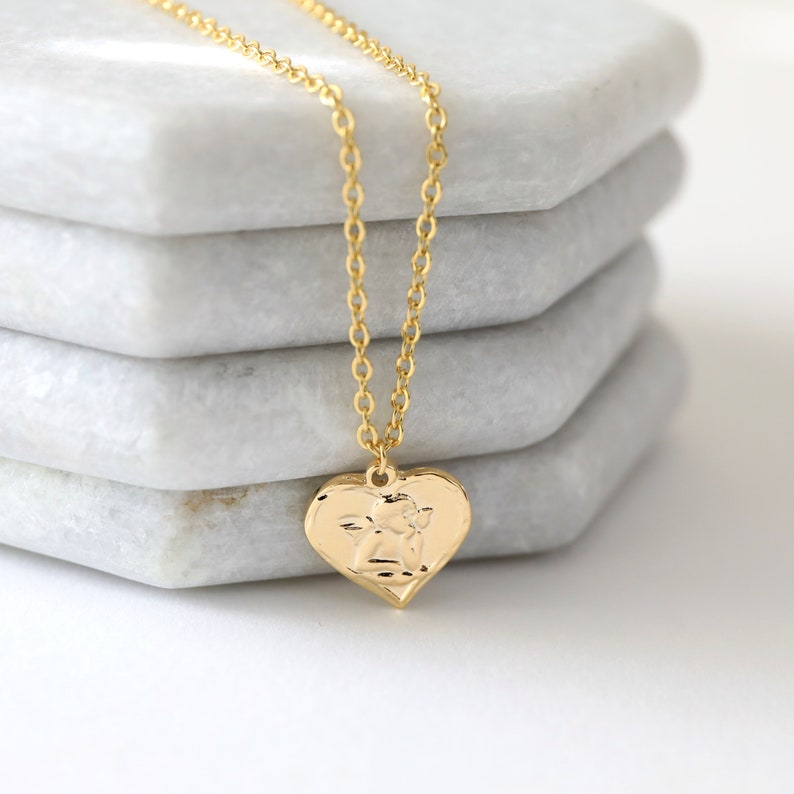 May include: A gold chain necklace with a heart-shaped pendant featuring an embossed angel design.