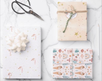 May include: Three gift boxes wrapped in different patterned paper. The first box is wrapped in white paper with gold stars and a red and white moon and stars design. The second box is wrapped in beige paper with gold stars and a green sprig of rosemary. The third box is wrapped in white paper with a colorful pattern of rainbows, ice cream cones, balloons, and stars.