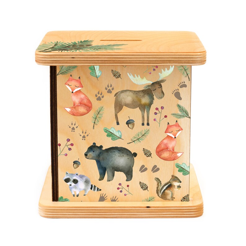 May include: Wooden piggy bank with a slot on top and a colorful woodland animal design. The design features a moose, fox, bear, raccoon, and squirrel.