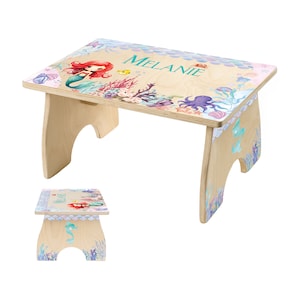 May include: A wooden step stool featuring a mermaid theme. The top surface is decorated with a mermaid illustration, coral, and the name "Melanie". The stool has a light wood finish with colorful aquatic designs.