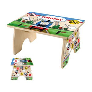 May include: A wooden children's table with a train theme. The tabletop features a blue train, the name "TIMOTHY", and railroad crossing signs. The legs are decorated with various road signs and train illustrations.