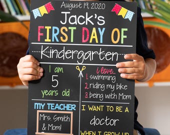 May include: A black chalkboard sign for the first day of kindergarten with colorful text and graphics. It displays the date August 19, 2020, the name Jack, age 5, interests including swimming, bike riding, and being with Mom, teacher Mrs. Smith, and career goal doctor.