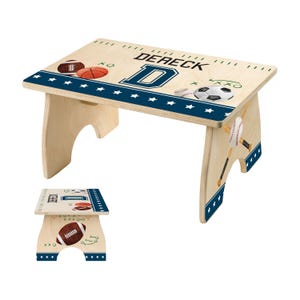 May include: A wooden step stool with a sports theme. The top features a football, basketball, and soccer ball design, along with the name "DERECK" and the letter "D". The edges are decorated with a blue border and white stars. Baseball and bat graphics are on the side.