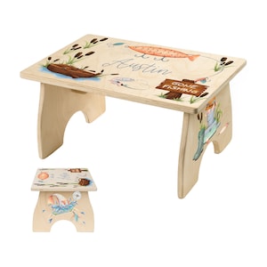 May include: A wooden step stool with a hand-painted design featuring a fishing scene. The stool is painted with a light wood stain and features a blue and white fish, a fishing rod, and a sign that says "Gone Fishing". The stool is personalized with the name "Austin".