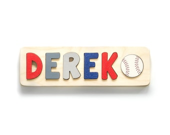 May include: Wooden puzzle spelling the name "DEREK" in red, grey, light grey, and blue letters. A baseball is on the right side. The puzzle is on a light wood base.