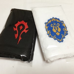 Pode incluir: Duas toalhas bordadas, uma preta com um símbolo da Horda vermelho e uma branca com um símbolo da Aliança azul.