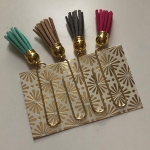 May include: Four gold bookmark clips with different colored tassels. The tassels are turquoise, brown, gray, and pink.
