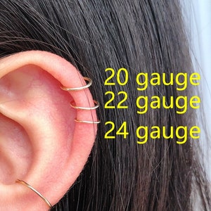 May include: Close-up of a person's ear with multiple gold hoop earrings in different sizes. The text "20 gauge", "22 gauge", and "24 gauge" is written on the right side of the image.