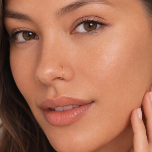 May include: A thin, circular gold nose ring hoop with a smooth, polished finish. The jewelry is a simple, continuous band design that sits flush against the skin. The text LUCKYJEWS is visible in the bottom right corner of the image.