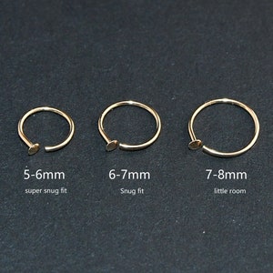 May include: Three gold-colored nose rings of varying sizes are displayed against a dark background. The rings are open-ended with a small, flat closure. Text indicates sizes: 5-6mm, 6-7mm, and 7-8mm, with fit descriptions.