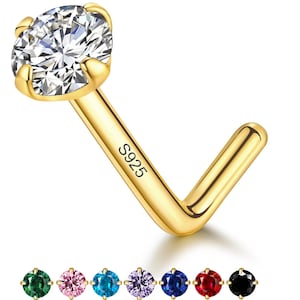 May include: A gold-colored nose ring with a clear, round gemstone. The nose ring is L-shaped with the text "S925" engraved on the stem. Additional gemstones in green, pink, blue, purple, dark blue, red, and black are shown.