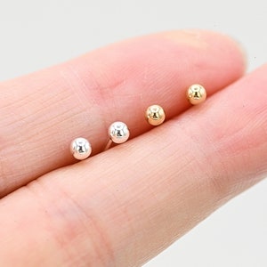May include: Three pairs of small, round stud earrings in silver, gold, and rose gold.