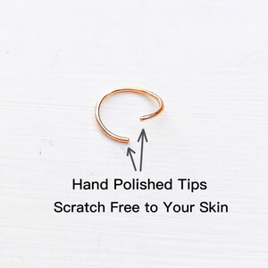 May include: A close-up of a gold nose ring with hand-polished tips. The ring is open and the ends are pointed towards the camera. The text "Hand Polished Tips" and "Scratch Free to Your Skin" is below the ring.