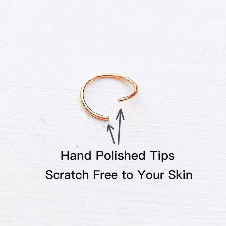 May include: A close-up of a gold nose ring with hand-polished tips. The ring is open and the ends are pointed towards the camera. The text "Hand Polished Tips" and "Scratch Free to Your Skin" is below the ring.