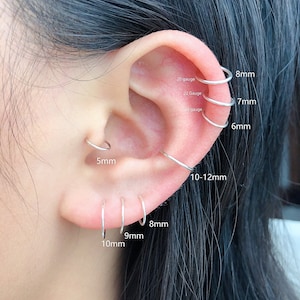 May include: An ear adorned with multiple silver hoop earrings, sized from 5mm to 10-12mm. The image highlights the gauge sizes: 20, 22, and 24. The earrings are shown on the ear, demonstrating different placement possibilities for the hoops.