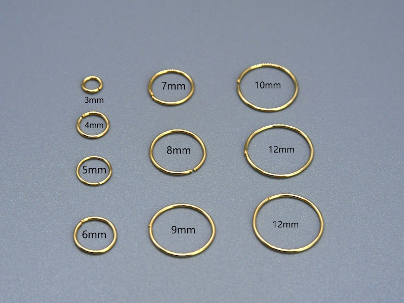 May include: A selection of gold-coloured hoop earrings in various sizes, ranging from 3mm to 12mm in diameter. Each earring is labelled with its size in millimetres, displayed against a grey background. The earrings are simple and elegant.