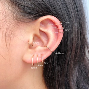 May include: An ear adorned with several gold hoop earrings of different diameters. The image shows the sizes: 5mm, 6mm, 7mm, 8mm, 9mm, 10mm, and 10-12mm. The gauges are 20, 22, and 24. The ear is shown in close-up.
