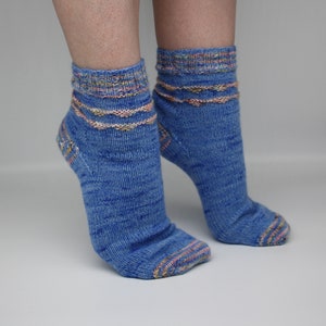 Pode incluir: Um par de meias azuis de tornozelo com listras coloridas ao redor da parte superior das meias.