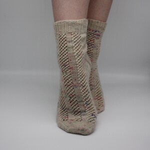 May include: A pair of beige socks with a colorful flecked yarn. The socks have a lacy pattern on the front and back.