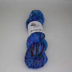 Op de afbeelding: Een bol blauwe, paarse en groene garen met een wit label waarop "Bumpy Yarn" staat.