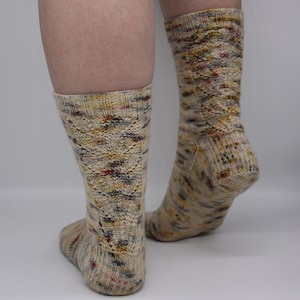 Peut inclure: Une paire de chaussettes beiges avec un motif moucheté coloré. Les chaussettes sont en tissu tricoté doux et ont une coupe confortable.