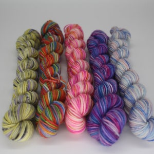 Puede incluir: Cinco ovillos de hilo de colores, cada uno con un patrón de color diferente. El hilo está dispuesto en una fila, con los colores que pasan del amarillo al azul.