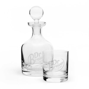 Puede incluir: Una jarra de cristal transparente con tapón redondo y un vaso a juego. Ambos presentan el texto grabado "Dr. Brewer Est. 2019". La jarra es alta y esbelta, mientras que el vaso es corto y ancho. El juego es ideal para servir bebidas.