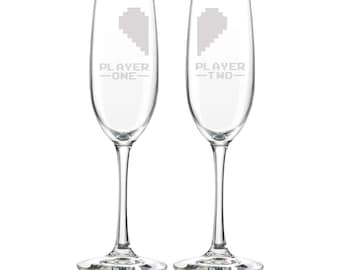 Könnte beinhalten: Zwei Champagnerflöten mit gravierten pixelartigen Herzen und dem Text "Player One" und "Player Two" auf jedem Glas.