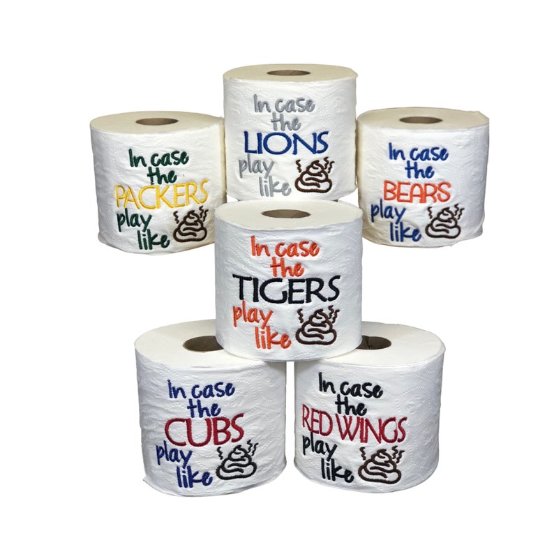May include: Six rolls of toilet paper with embroidered text on each roll. The text reads "In case the [Team Name] play like [Poop Emoji]" with the team names being Packers, Lions, Tigers, Bears, Cubs, and Red Wings.