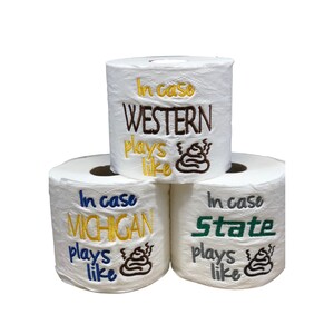 May include: Three rolls of toilet paper with embroidered text. The top roll says "In case WESTERN plays like" with a brown poop emoji. The middle roll says "In case MICHIGAN plays like" with a brown poop emoji. The bottom roll says "In case State plays like" with a brown poop emoji.