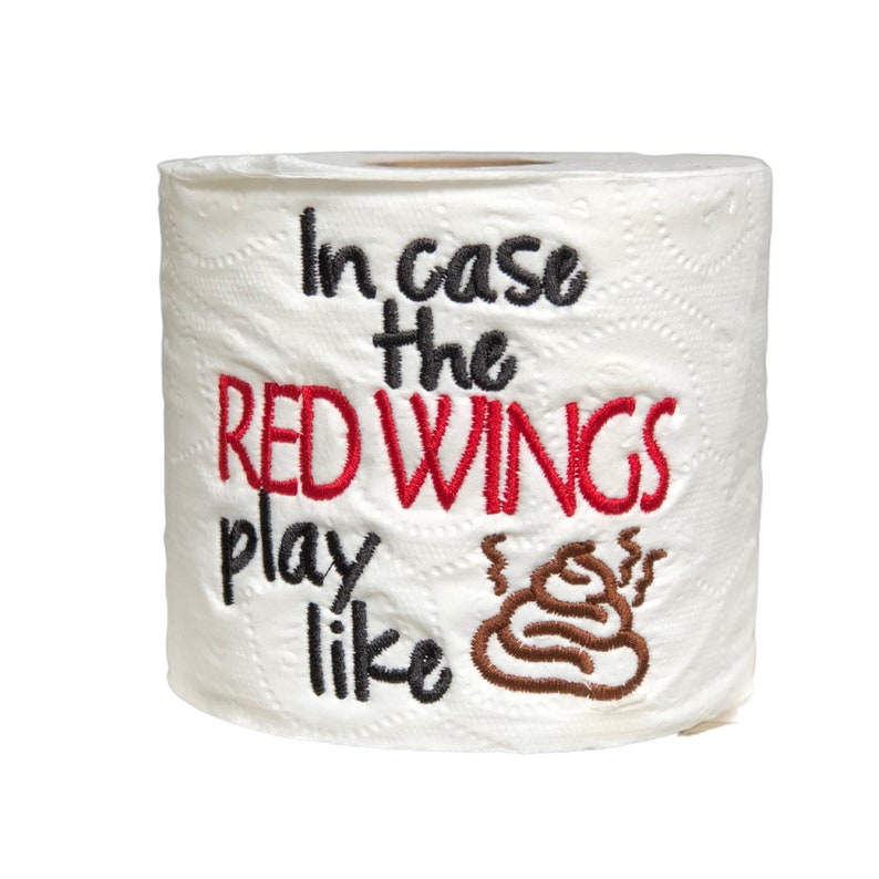May include: A white toilet paper roll with the text "In case the Red Wings play like" embroidered on it. A brown poop emoji is embroidered next to the text.