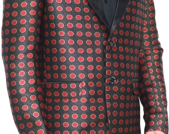 Puede incluir: Un blazer negro con un patrón repetitivo de círculos rojos con bordes dorados. La chaqueta incluye una solapa de chal en satén negro, dos botones negros en el cierre frontal y dos bolsillos horizontales con solapas negras en la parte inferior.