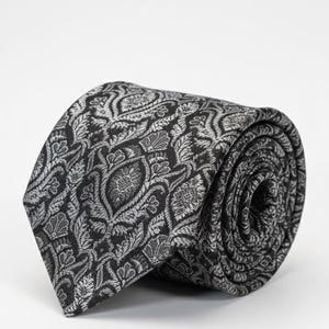 May include: A rolled-up black tie with a silver floral design. The tie, made from textured fabric, is set against a white backdrop. The detailed pattern features stylized flowers and leaves.