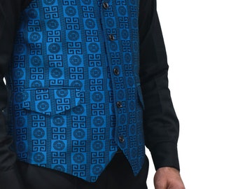 May include: A vibrant blue vest featuring a repeating black geometric Greek key pattern. The garment includes a notched lapel, a single-breasted front with five dark buttons, and two front pockets with flaps, worn over a solid black shirt.