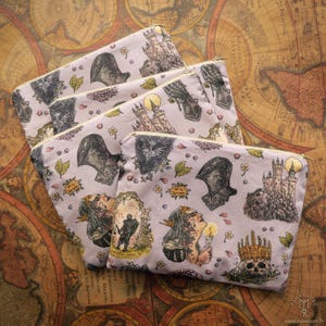 Puede incluir: Conjunto de cinco bolsas con cremallera de color morado con un patrón repetido de una mujer con una corona, un caballero, un castillo y flores. Las bolsas están hechas de un material suave de tela.